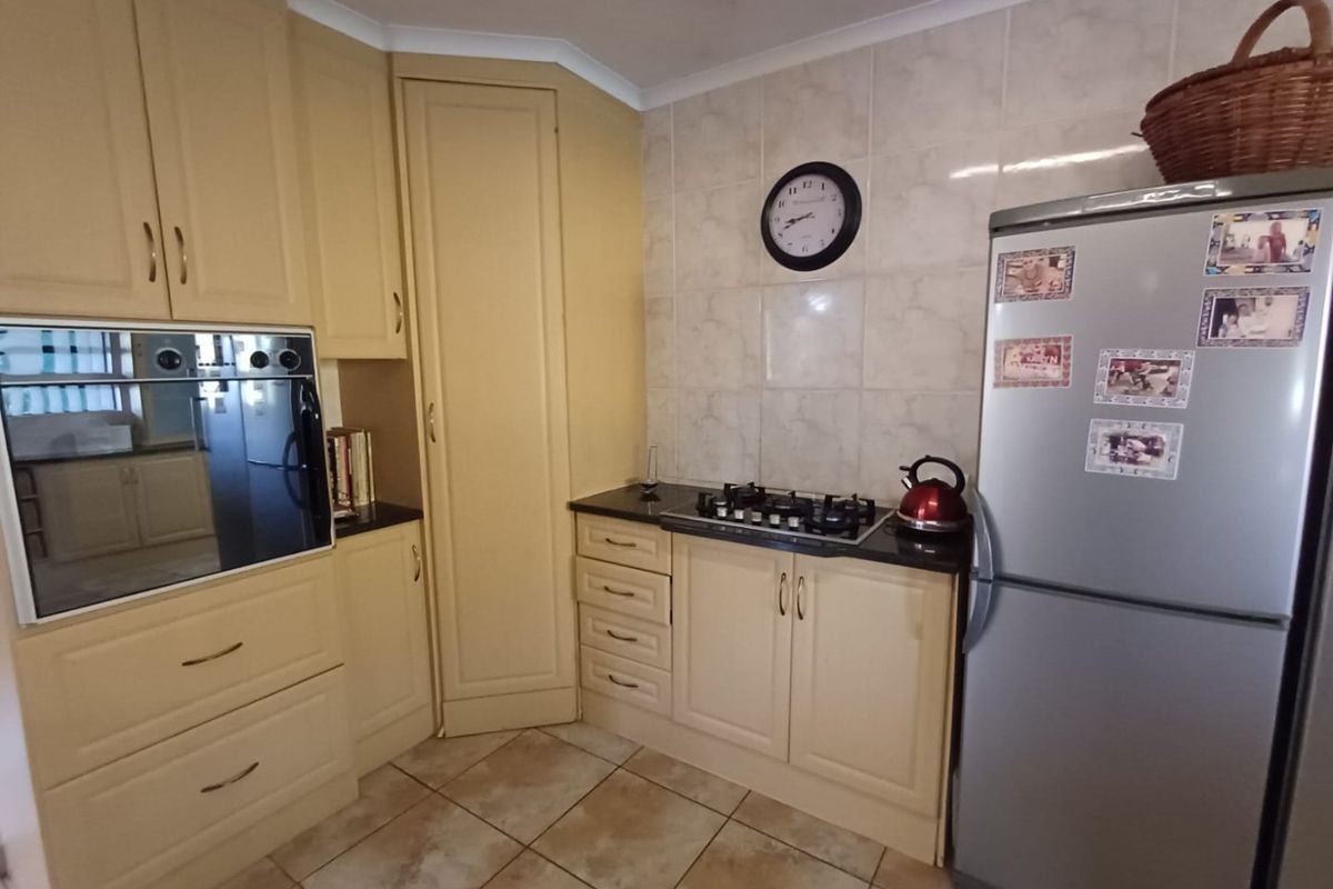 A functional kitchen featuring cream-colored cabinetry, granite countertops, a gas hob, and a built-in oven with tiled splashbacks and flooring.