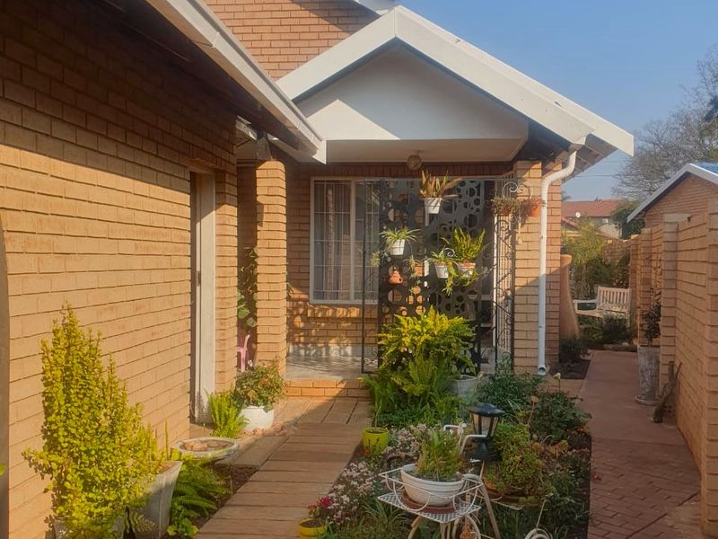 A well-maintained rear exterior view featuring a brick facade, paved walkway, and established garden beds along the side of the house.