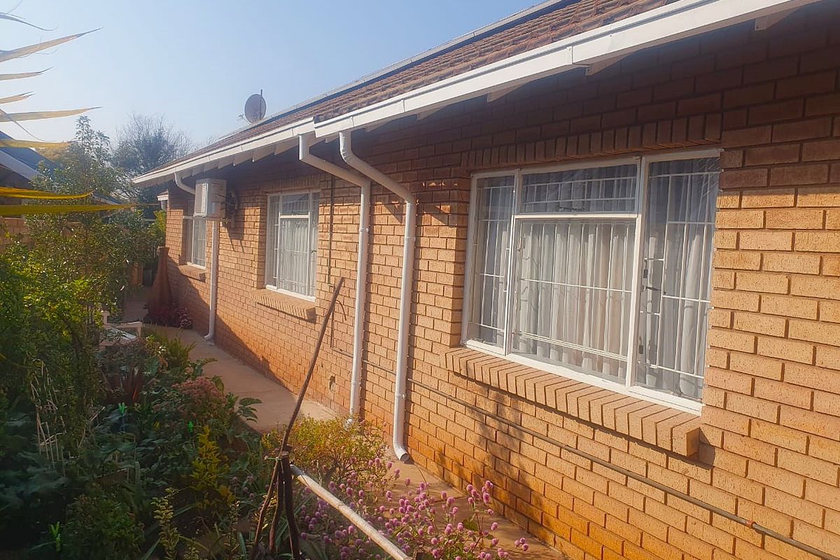 Rear elevation of a face brick house featuring white aluminium window frames with security bars, gutters, and an external air conditioning unit.