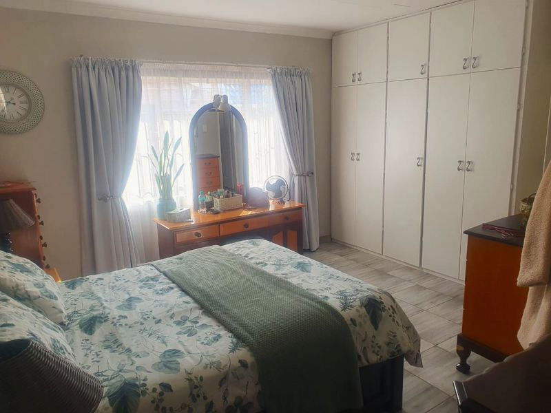 A well-lit bedroom featuring neutral walls, tiled flooring, and extensive floor-to-ceiling built-in cupboards providing ample storage space.