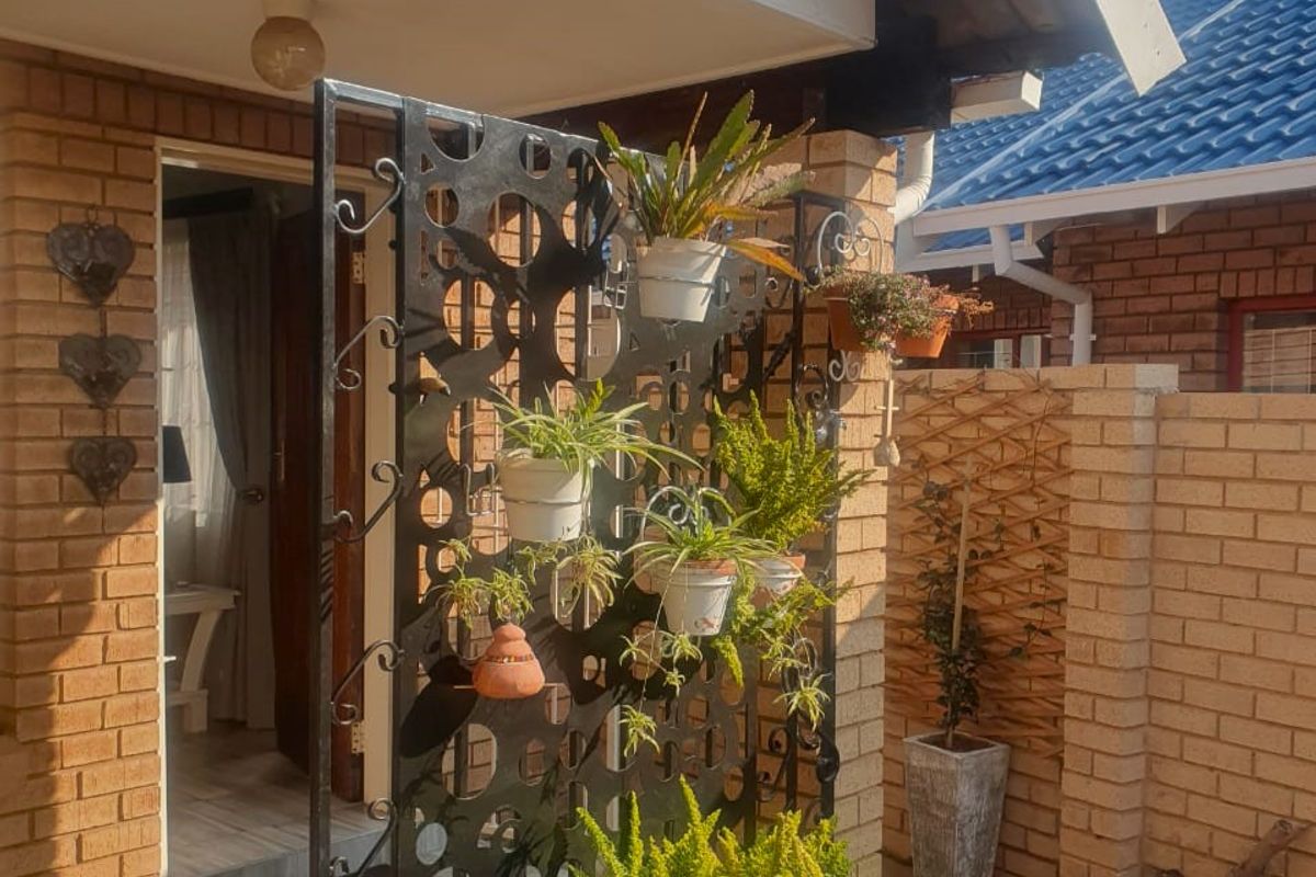 A covered patio entrance featuring brick walls, tiled flooring, and a decorative metal privacy screen with integrated plant displays.