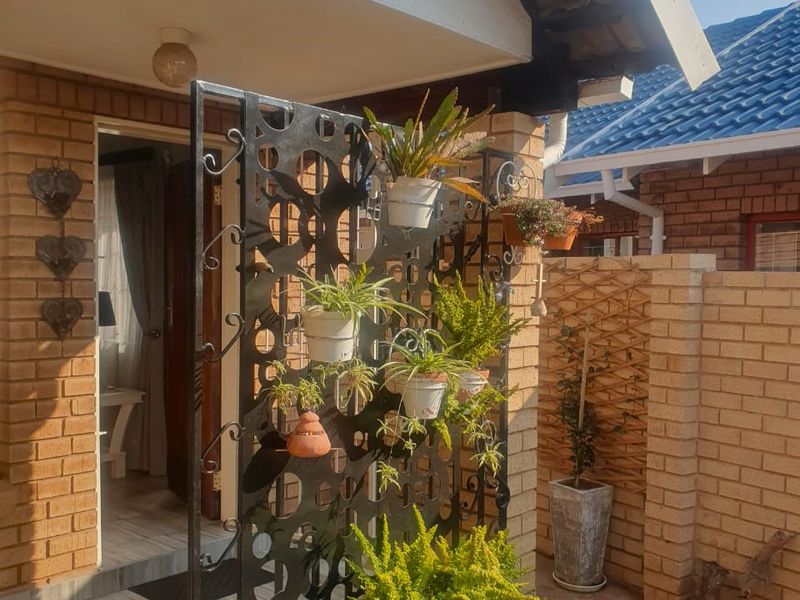 A covered patio entrance featuring brick walls, tiled flooring, and a decorative metal privacy screen with integrated plant displays.