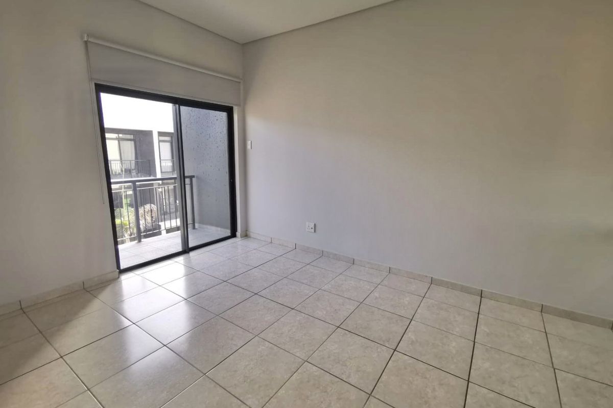 A bright, empty bedroom featuring neutral tiled flooring and a sliding glass door providing access to a private balcony.