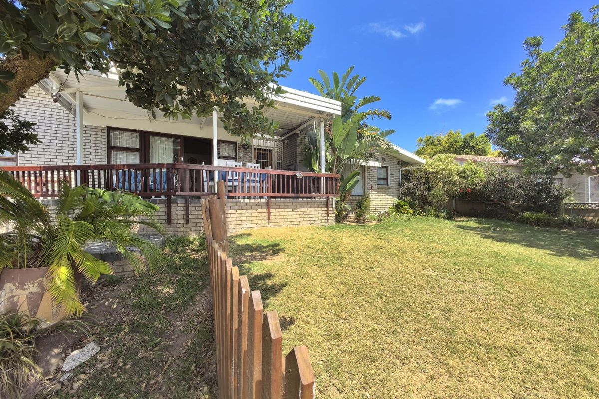 Rear view of the property featuring a covered patio with a timber deck, overlooking a private garden and lawn area.