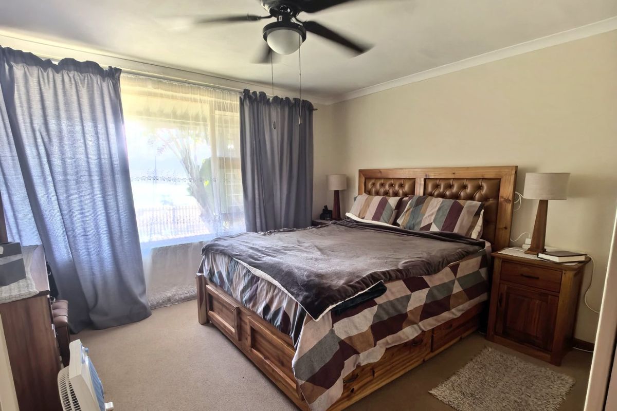 A comfortable bedroom featuring a ceiling fan, carpeted flooring, and a large window allowing for natural light.