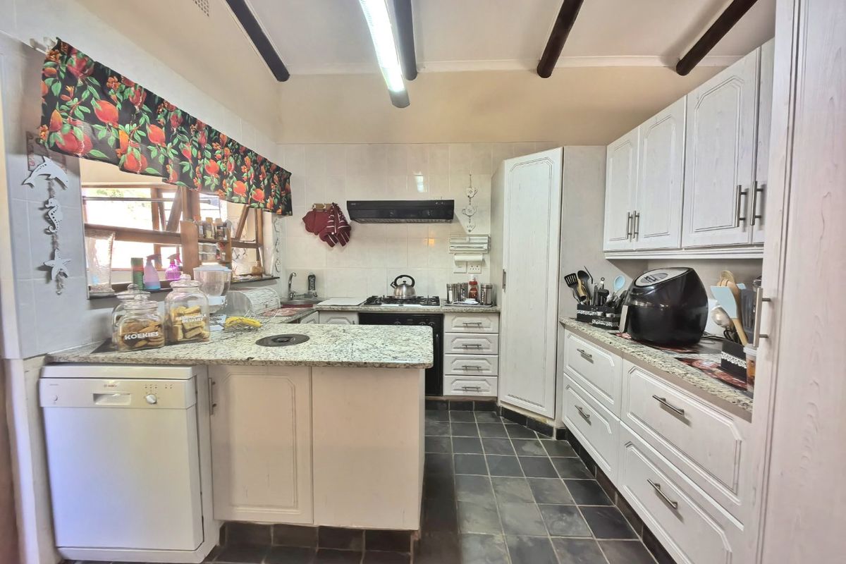 Functional kitchen featuring granite countertops, white cabinetry, exposed ceiling beams, and a gas hob with an integrated extractor fan.