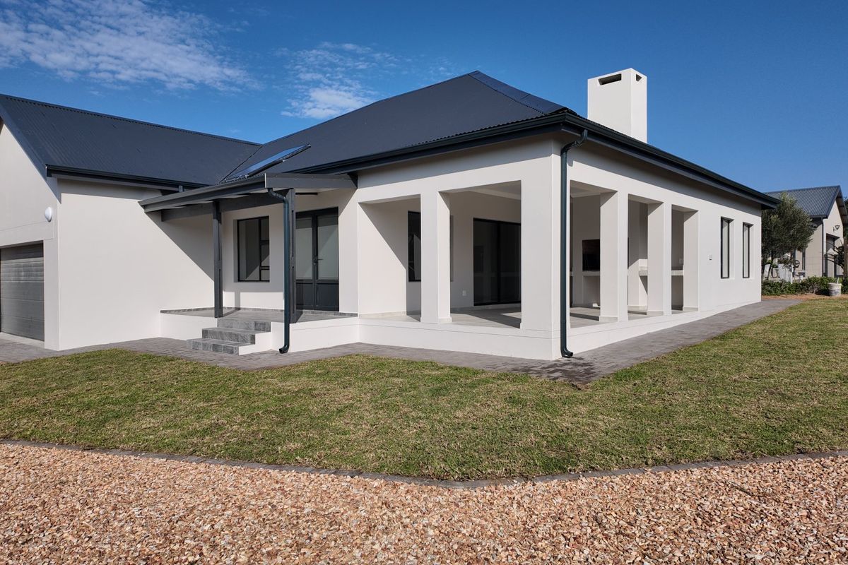 Rear view of a modern house featuring a covered patio with a built-in braai, paved walkways, and a well-maintained lawn.