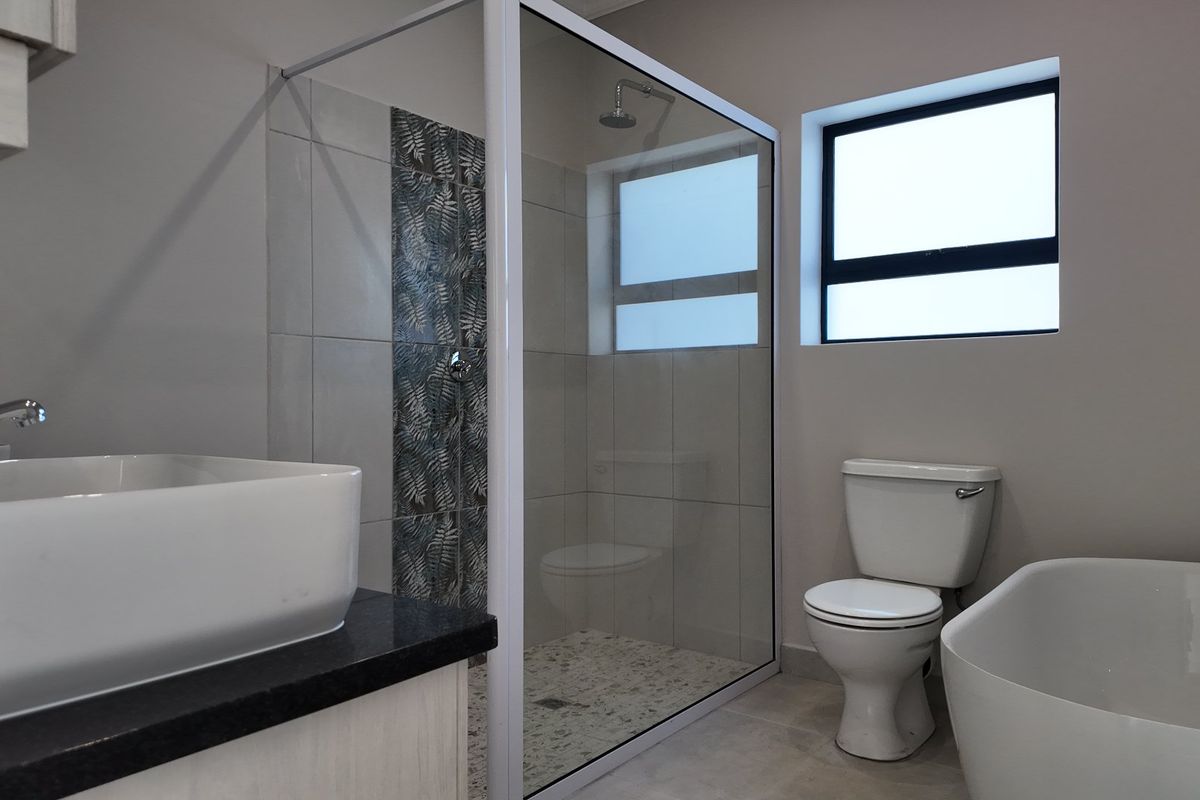Modern bathroom featuring a glass-enclosed shower, a sleek freestanding bathtub, a vessel sink vanity, and neutral tiling.