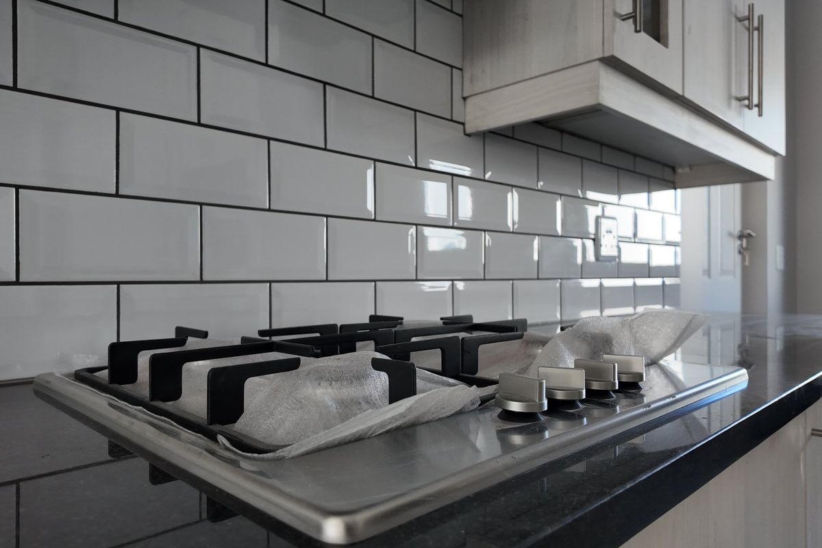 Modern kitchen featuring a sleek gas hob, dark granite countertops, and a clean white subway tile backsplash.