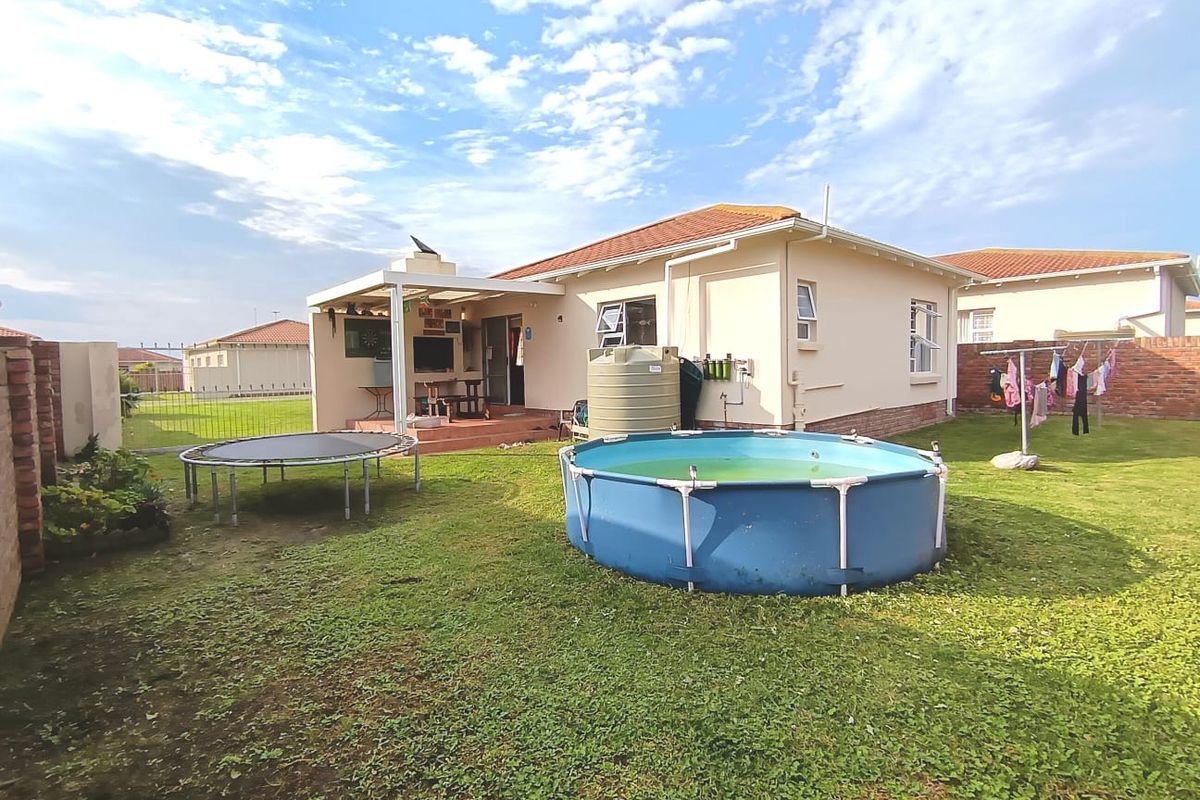 Rear view of the townhouse featuring a covered patio with a built-in braai, a water storage tank, and a spacious garden area.