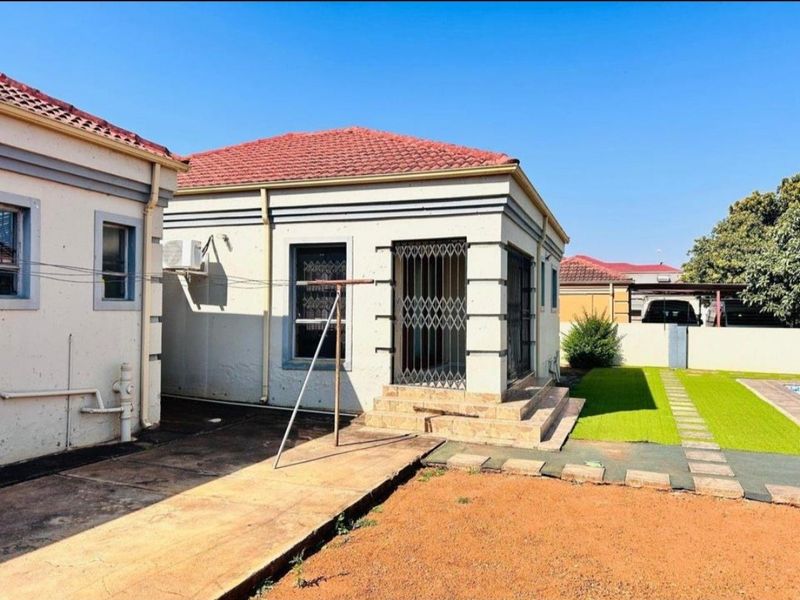 Rear view of the property featuring a tiled roof, security gate, paved walkway, and a small artificial lawn area.