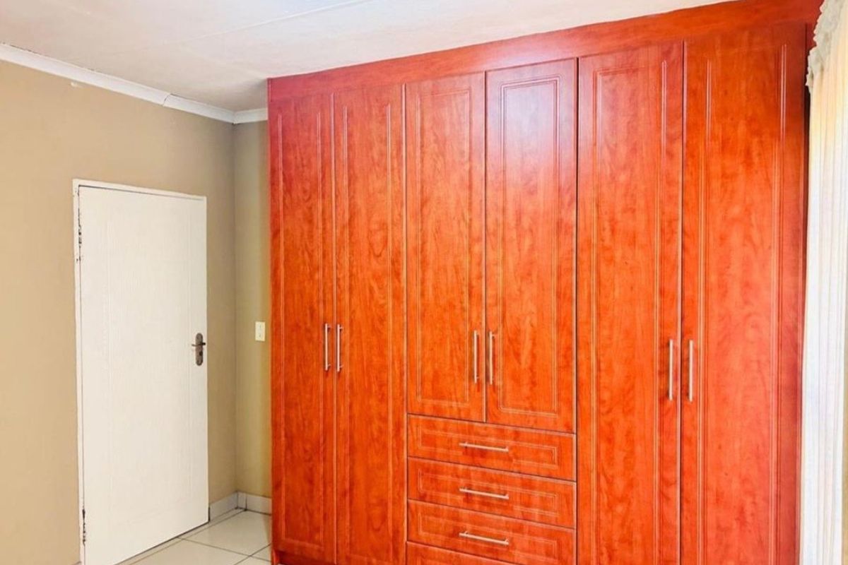 A clean bedroom featuring extensive floor-to-ceiling built-in wooden cupboards and neutral tiled flooring.