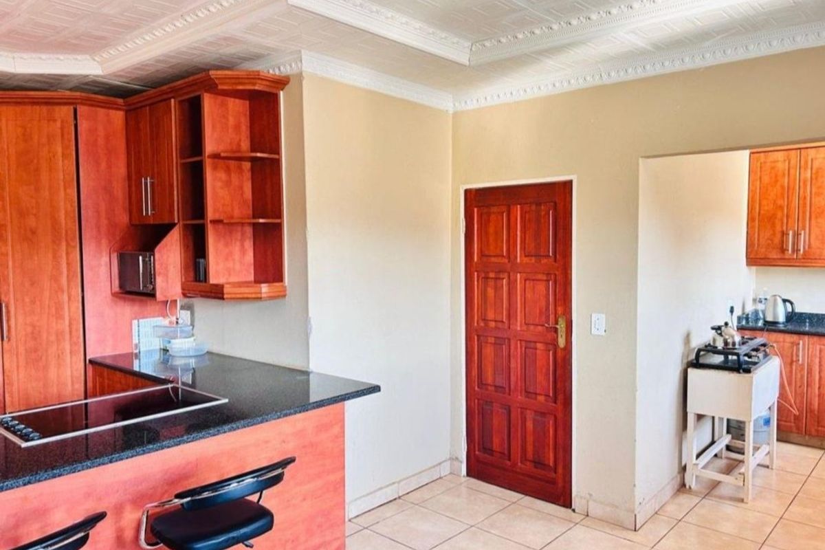 Kitchen featuring wooden cabinetry, granite countertops, an integrated hob, and decorative ceiling tiles, with an adjacent scullery area.
