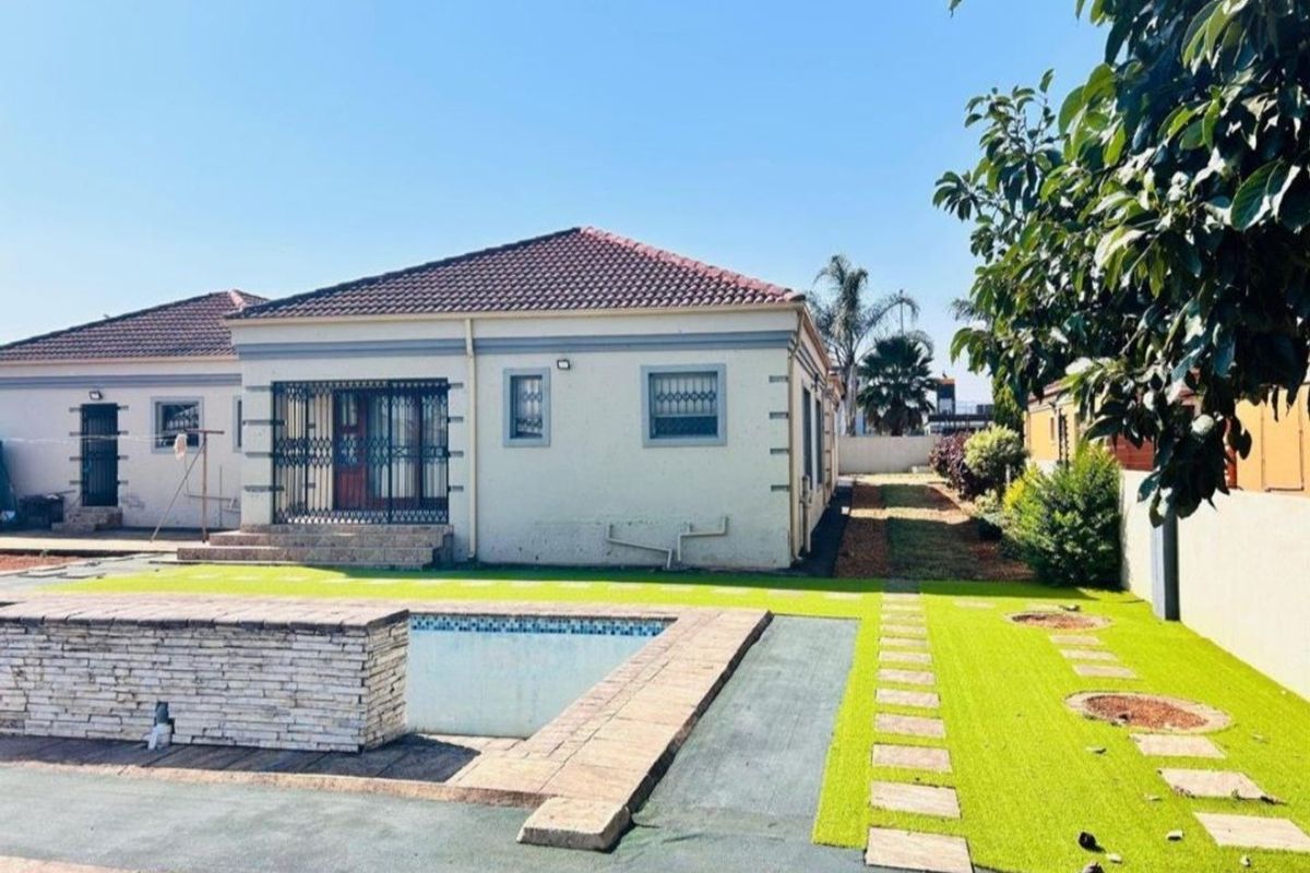 Rear view of the property featuring a swimming pool with a stone-clad feature wall, artificial lawn, and paved pathways.