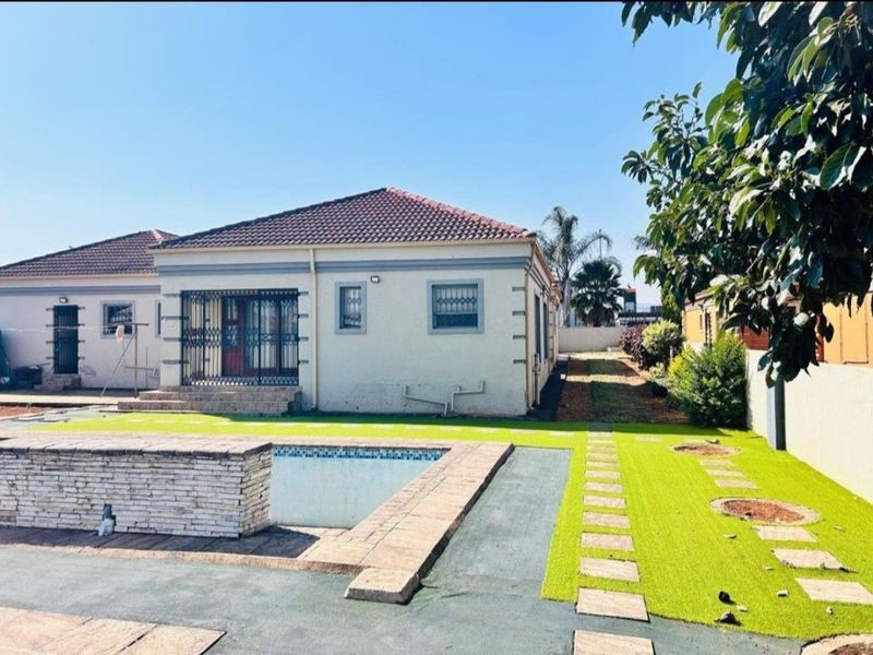 Rear view of the property featuring a swimming pool with a stone-clad feature wall, artificial lawn, and paved pathways.