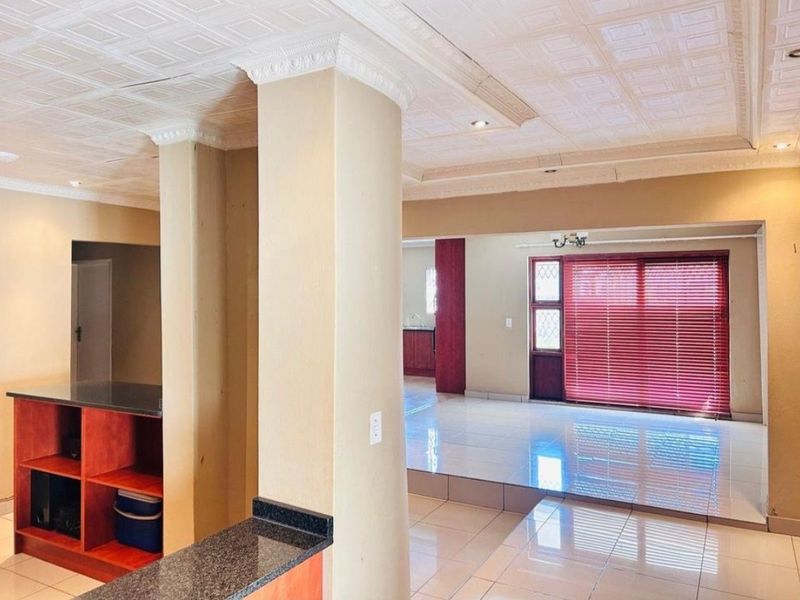 Spacious open-plan living area featuring tiled floors, a coffered ceiling, and built-in cabinetry with granite countertops, leading to a bright outdoor access point.