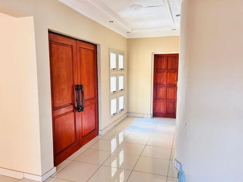A bright and spacious entrance hall featuring polished tiled flooring, decorative ceiling detailing, and classic timber doors.