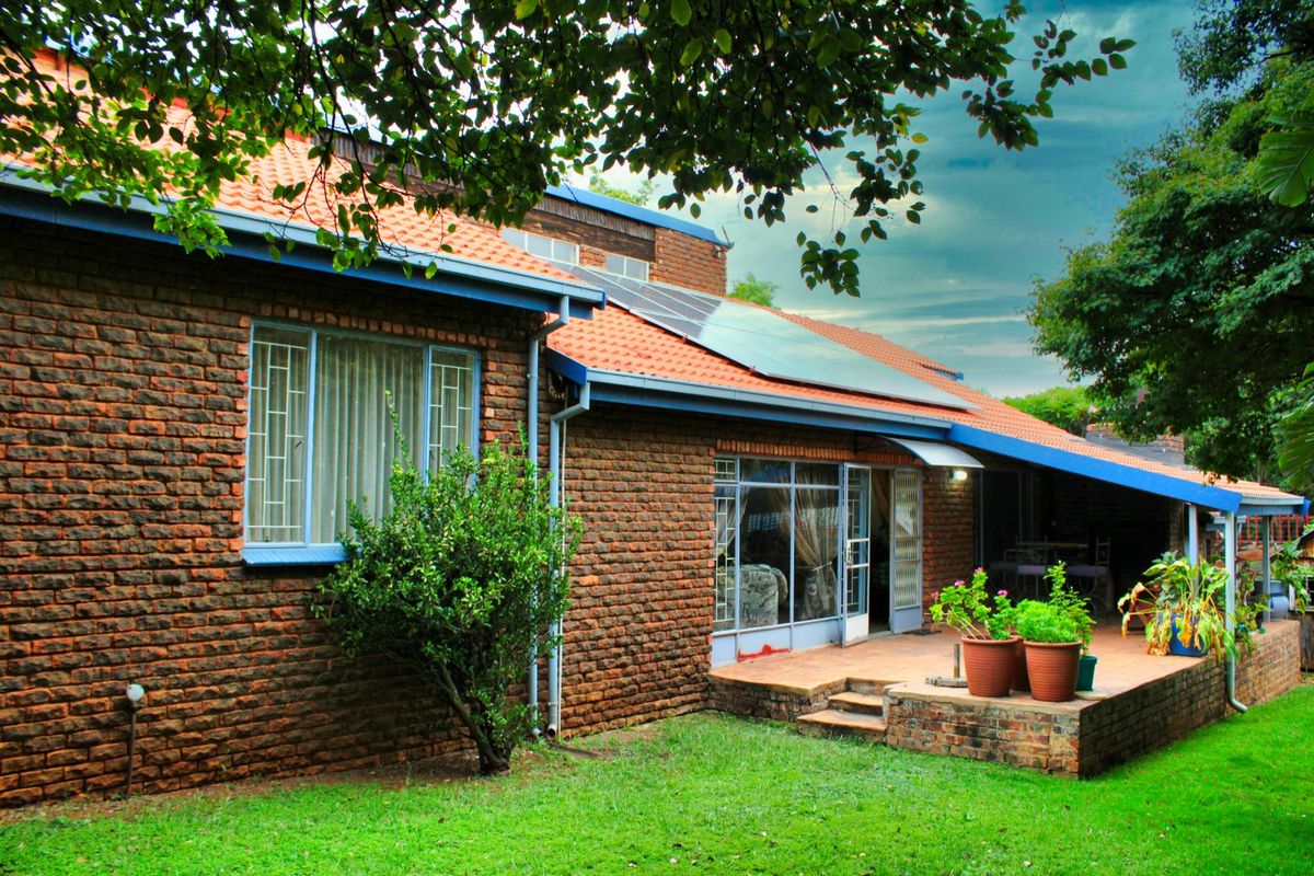Rear view of the house featuring exposed brickwork, a terracotta tiled roof with solar panels, and a covered patio area overlooking the garden.
