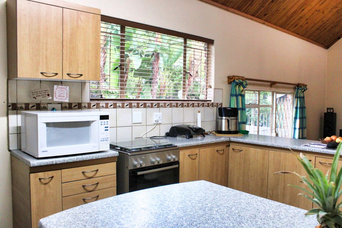 A functional kitchen featuring light wood cabinetry, granite countertops, a tiled backsplash, and a vaulted timber ceiling with natural light.