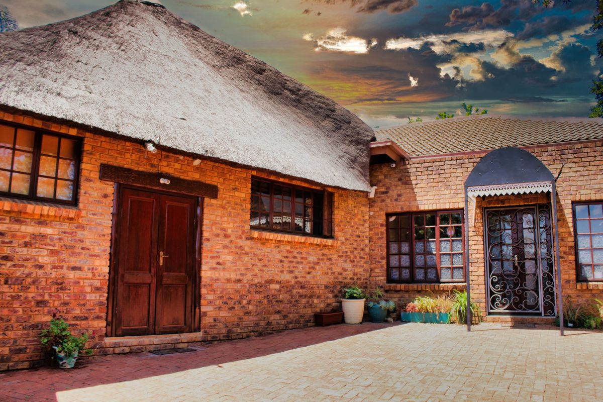 A rear courtyard view featuring a traditional thatch roof, face brick exterior, and secure timber and wrought iron entrance doors.