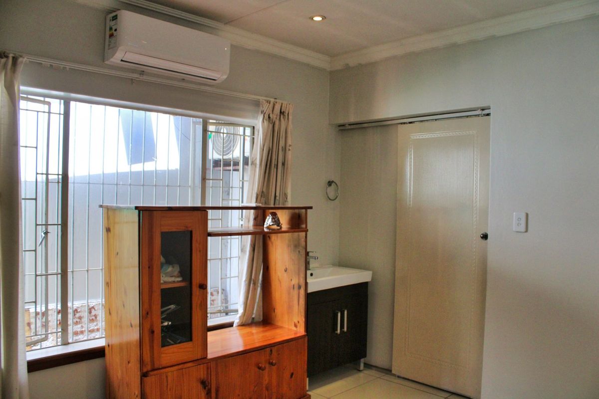Bedroom featuring a built-in vanity basin, split-system air conditioning, tiled flooring, and a sliding door with security bars on the window.