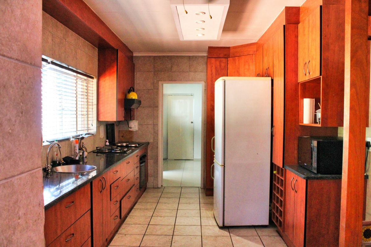 A functional kitchen featuring warm-toned wooden cabinetry, granite countertops, a gas hob, and tiled finishes, offering a practical layout with ample storage space.