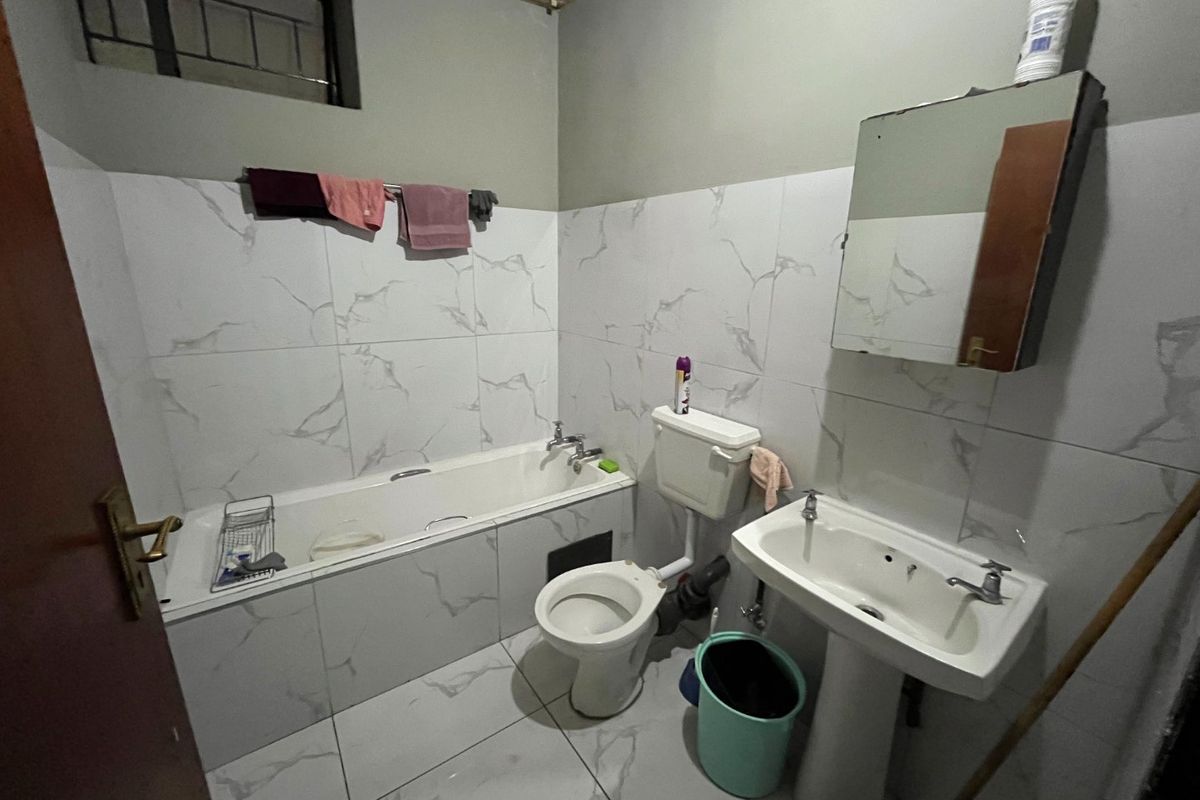 A functional bathroom featuring a bathtub, pedestal basin, and toilet with marble-effect wall tiling and exposed plumbing elements.