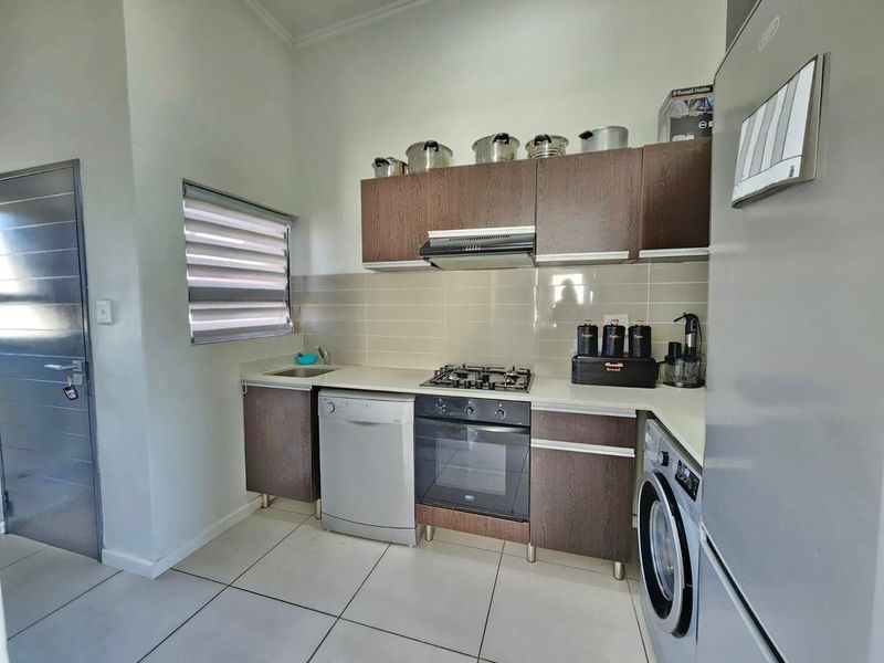 Compact kitchen featuring dark wood cabinetry, gas hob, built-in oven, extractor fan, and tiled flooring with a neutral backsplash.