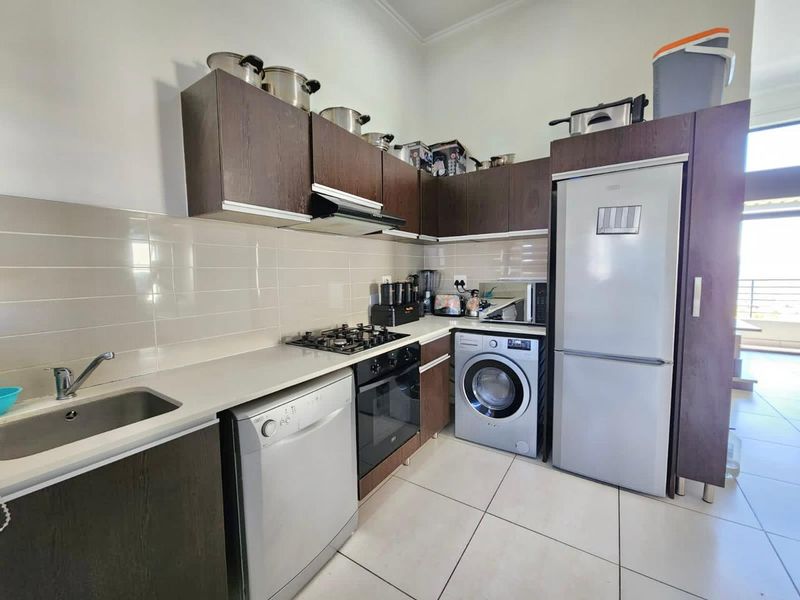 A functional kitchen featuring dark wood cabinetry, a gas hob, electric oven, extractor fan, and tiled backsplash with integrated appliance spaces.