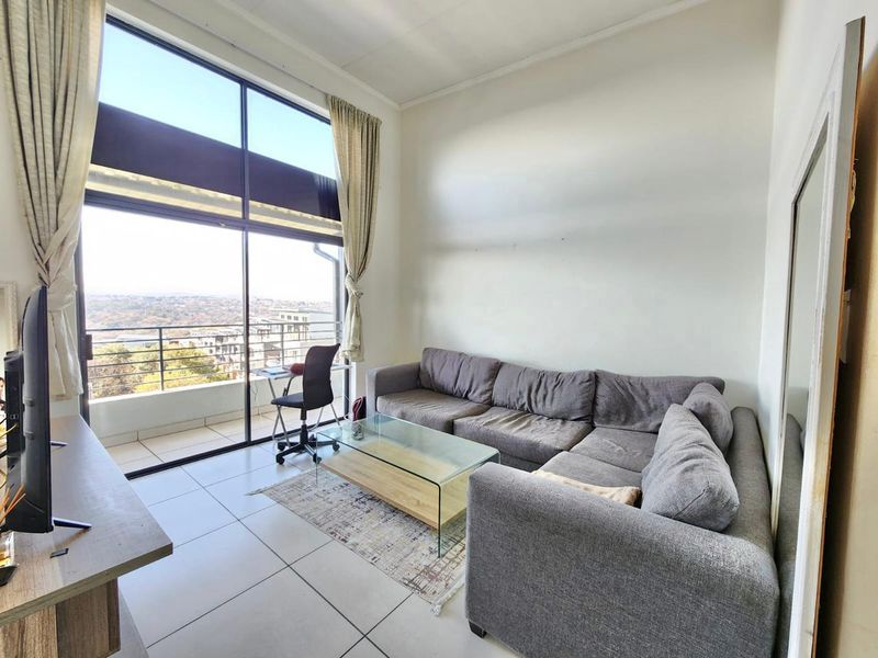 A bright living room featuring large floor-to-ceiling windows, tiled flooring, and direct access to a balcony with expansive views.