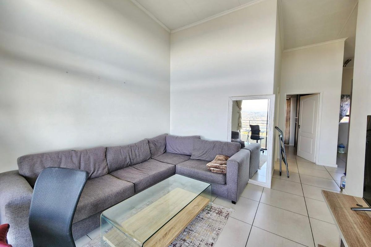 A spacious living area featuring high ceilings and neutral tiled flooring, providing a bright and open atmosphere with access to adjacent rooms.