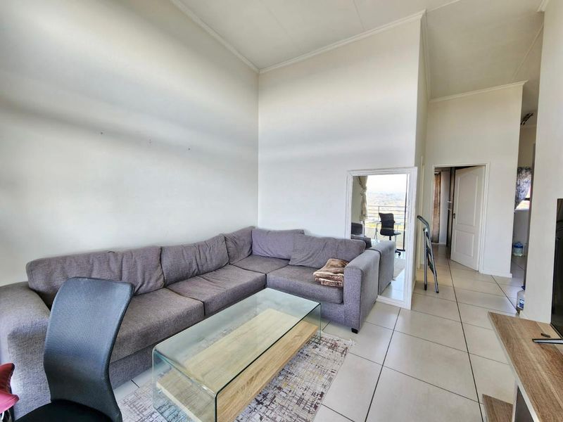 A spacious living area featuring high ceilings and neutral tiled flooring, providing a bright and open atmosphere with access to adjacent rooms.