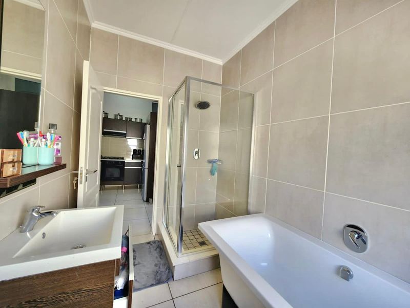 A modern bathroom featuring a glass shower enclosure, a freestanding bathtub, and a vanity basin with neutral wall and floor tiling.