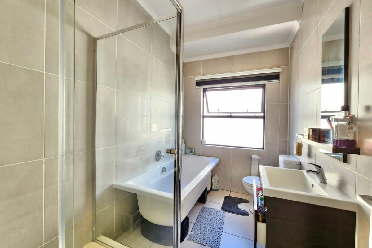 A well-maintained bathroom featuring a freestanding bathtub, glass shower screen, modern vanity cabinet, and neutral wall tiling.