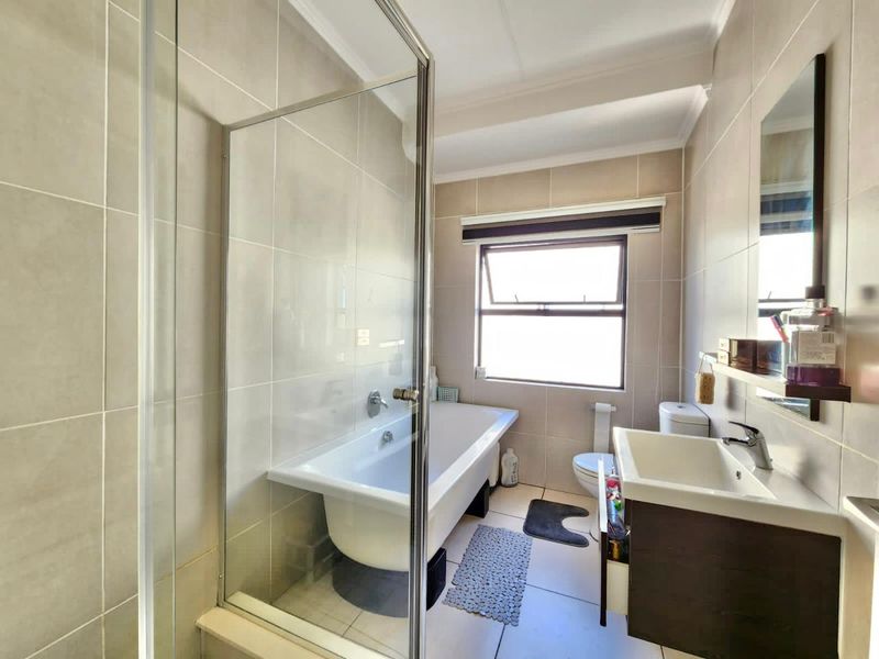 A well-maintained bathroom featuring a freestanding bathtub, glass shower screen, modern vanity cabinet, and neutral wall tiling.