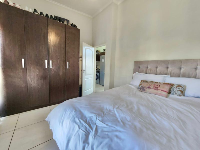 A well-maintained bedroom featuring large built-in wooden wardrobes, neutral tiled flooring, and direct access to an adjacent utility area.