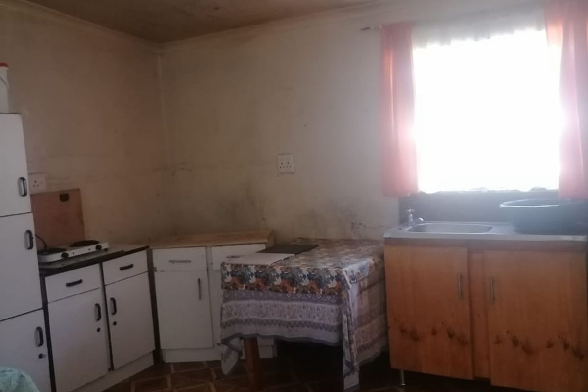 A dated kitchen featuring basic cabinetry, a stainless steel sink, and tiled flooring, requiring cosmetic updates and wall repairs.