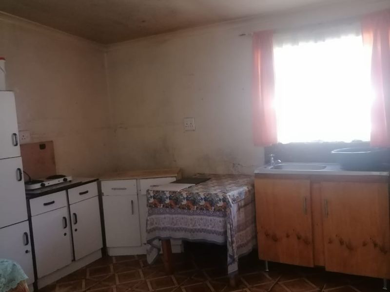 A dated kitchen featuring basic cabinetry, a stainless steel sink, and tiled flooring, requiring cosmetic updates and wall repairs.