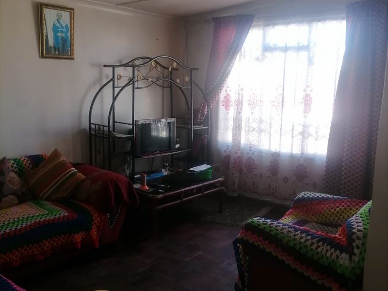 A living room featuring parquet flooring and a large window, currently showing signs of wear and requiring cosmetic updates to improve its overall appeal.