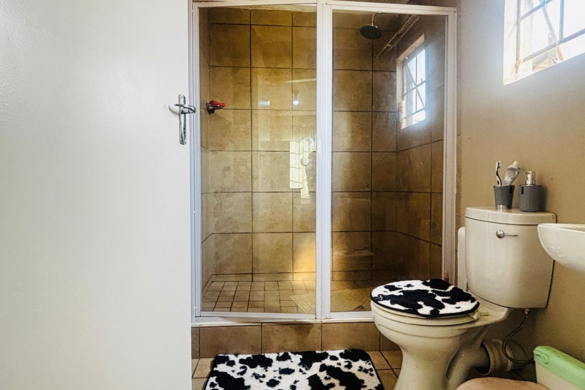 A functional bathroom featuring a tiled shower enclosure, standard toilet, and pedestal basin, offering a practical layout with potential for modern updates.