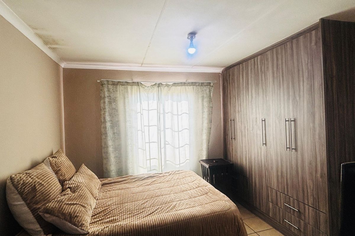 A bedroom featuring built-in wooden cupboards, tiled flooring, and coving, with visible ceiling water staining requiring attention.