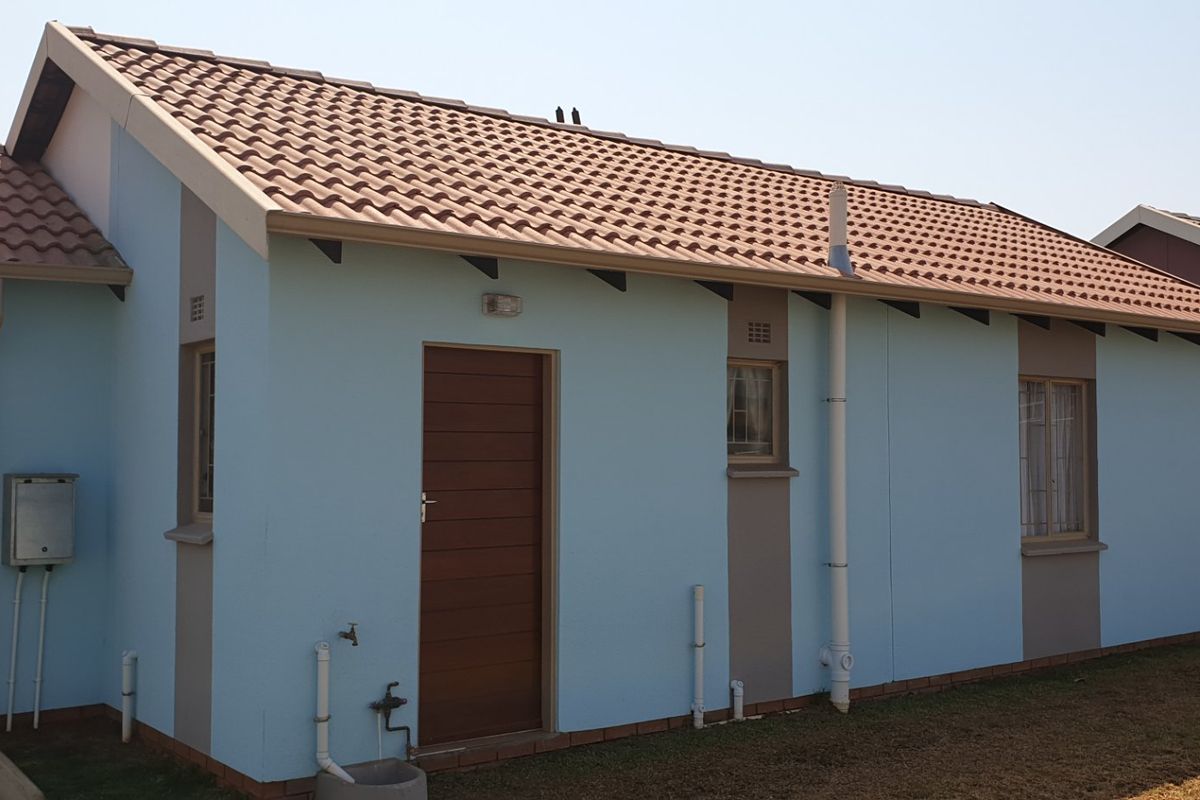 A view of the rear exterior of the house featuring a tiled roof, painted walls, and a secure external door.