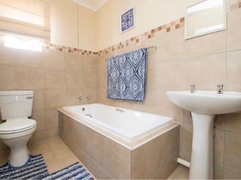 A functional bathroom featuring a pedestal basin, a built-in bathtub, and neutral ceramic wall and floor tiling.