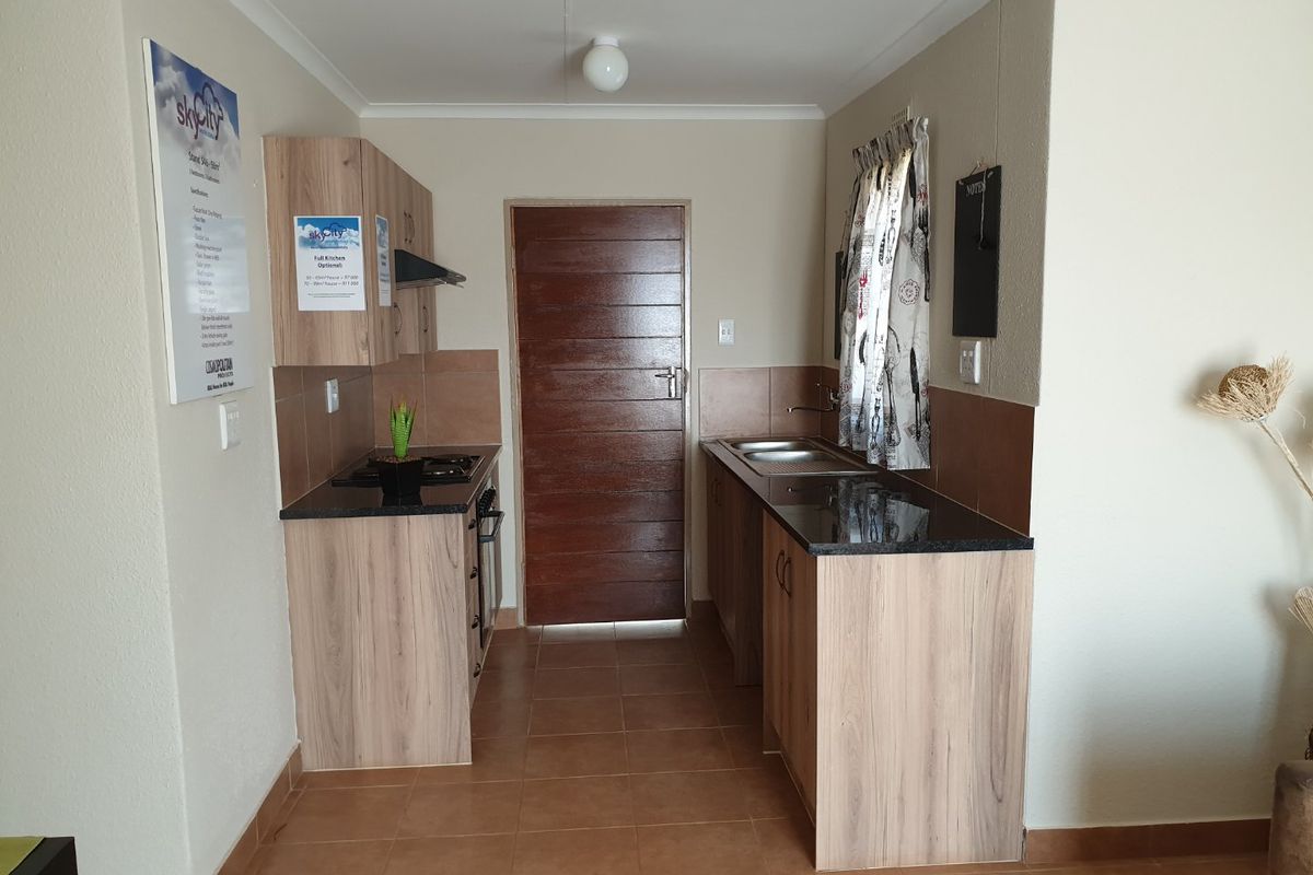 Compact kitchen featuring light wood-finish cabinetry, granite countertops, built-in hob and oven, and tiled flooring.