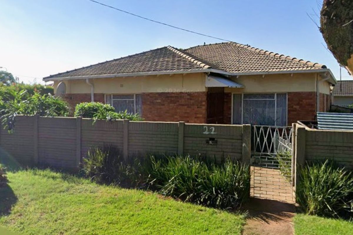 Front view of a single-story brick house featuring a tiled roof, enclosed by a precast concrete boundary wall with a metal pedestrian gate.