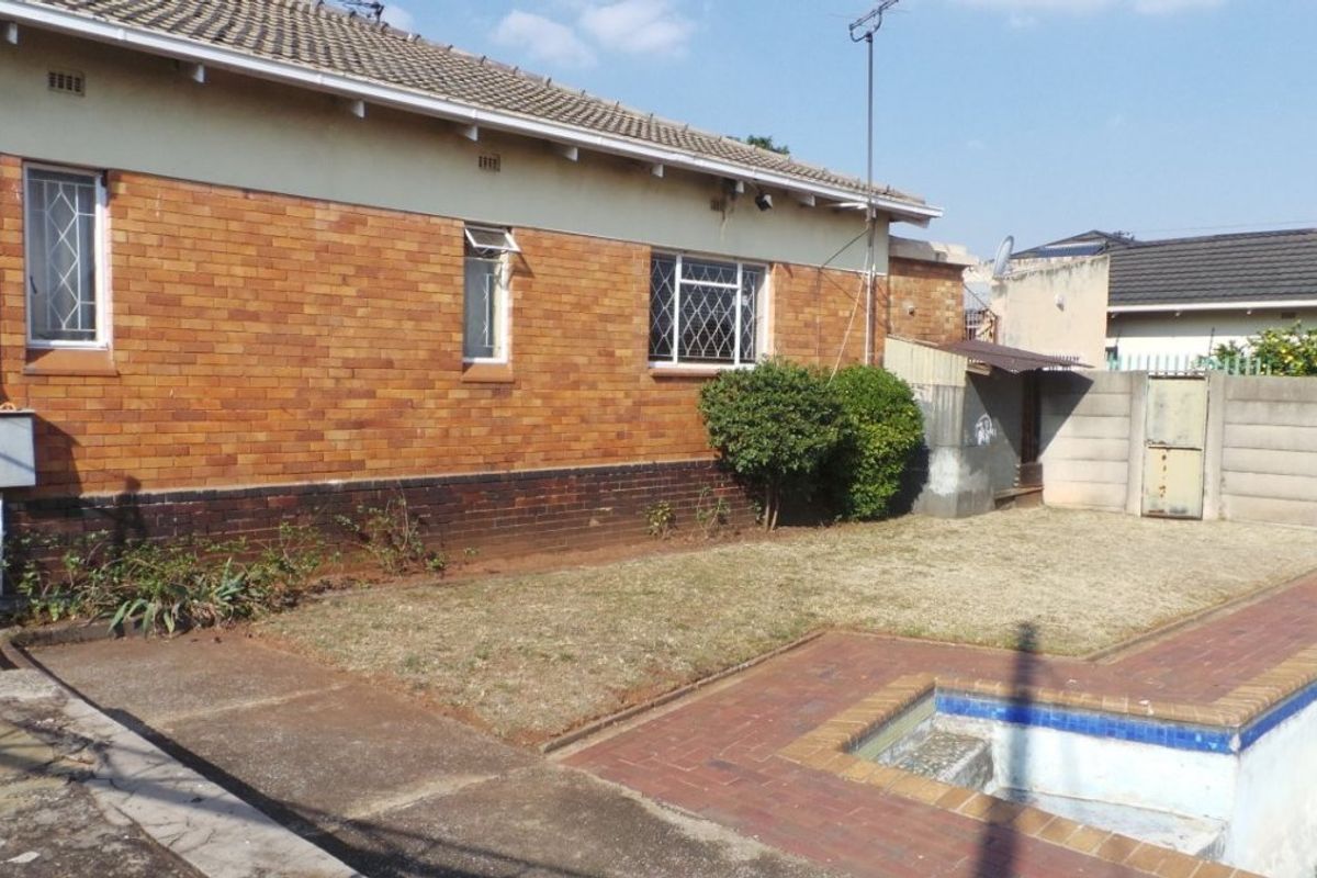 Rear exterior view of the house featuring a brick facade, swimming pool with brick paving, and a surrounding precast concrete boundary wall.