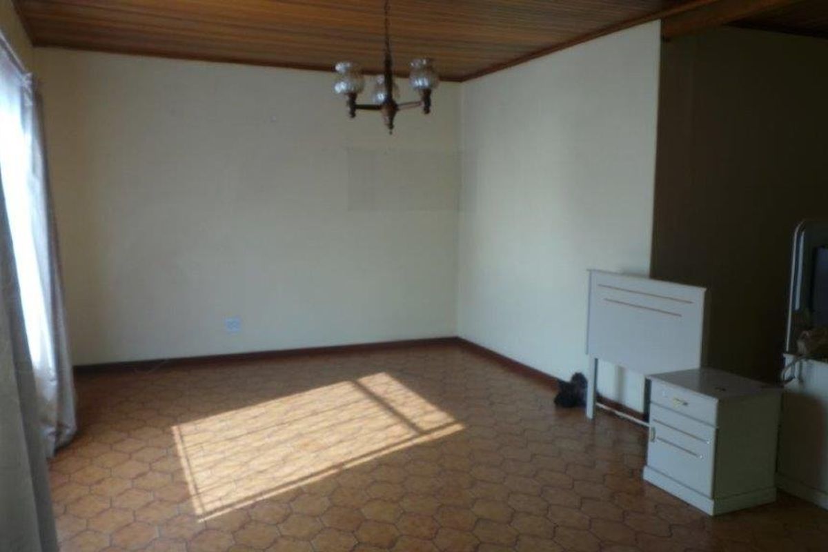 An empty living room featuring a timber-paneled ceiling and tiled flooring, offering a blank canvas for renovation and interior design updates.