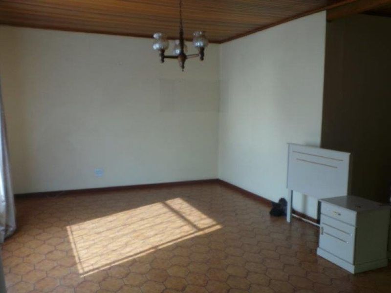An empty living room featuring a timber-paneled ceiling and tiled flooring, offering a blank canvas for renovation and interior design updates.