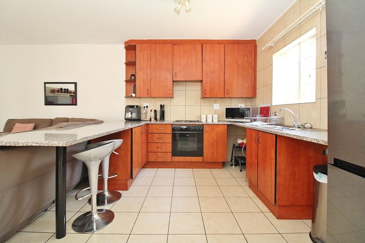 Open-plan kitchen featuring wooden cabinetry, granite countertops, a breakfast bar, and tiled flooring, seamlessly integrated with the living area.