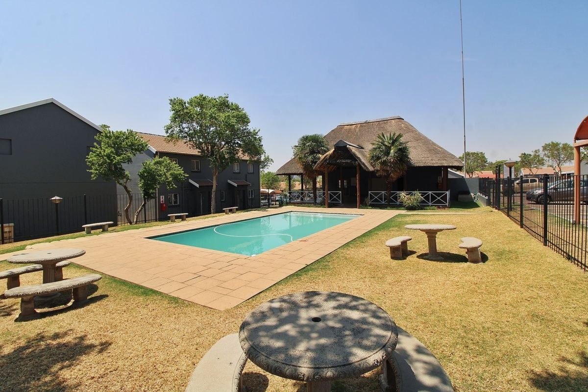 Communal pool area featuring a swimming pool, paved deck, and a traditional thatched lapa structure within a fenced complex.